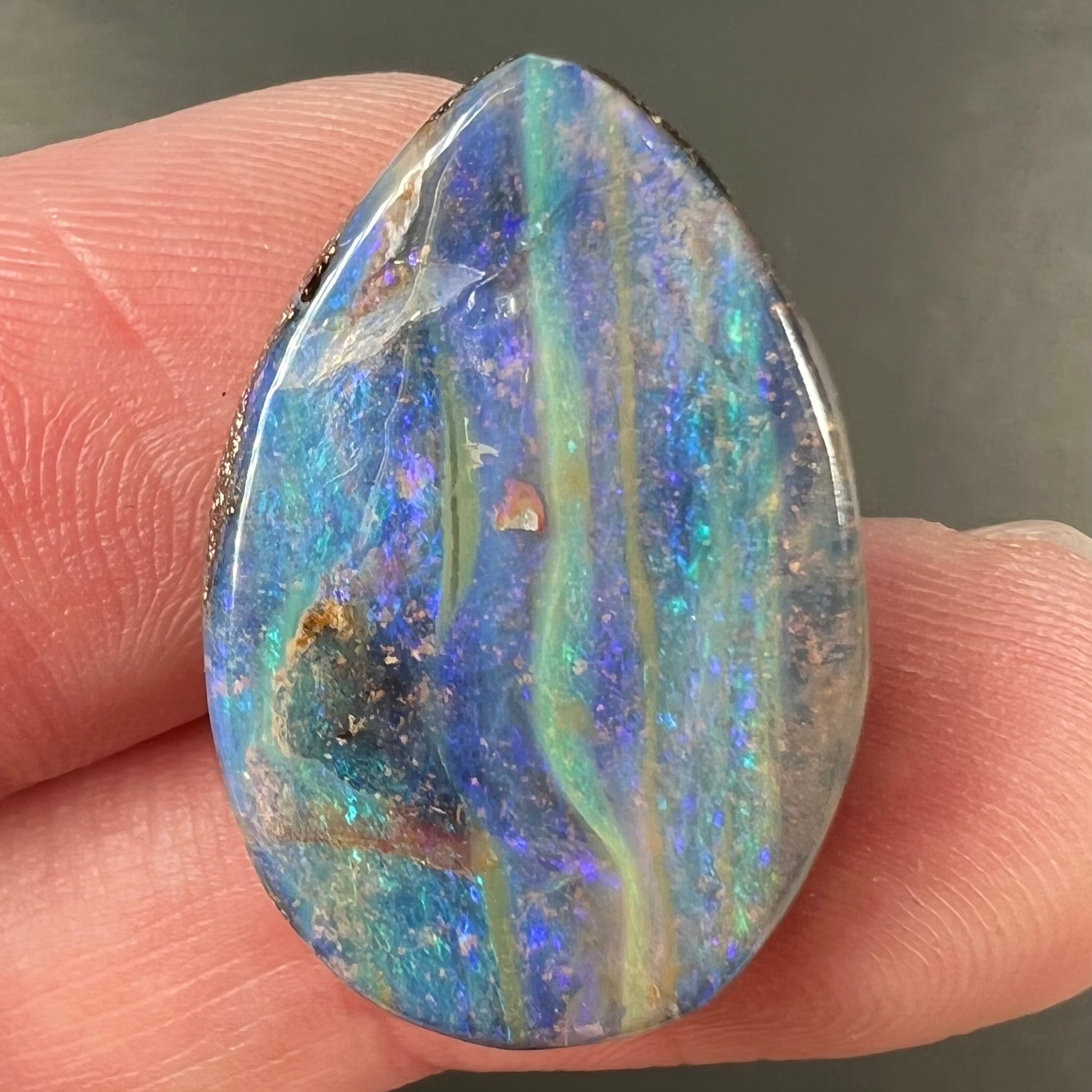 A loose, pear shaped Australian boulder opal stone.  The predominant colors are purple, green, and aqua.