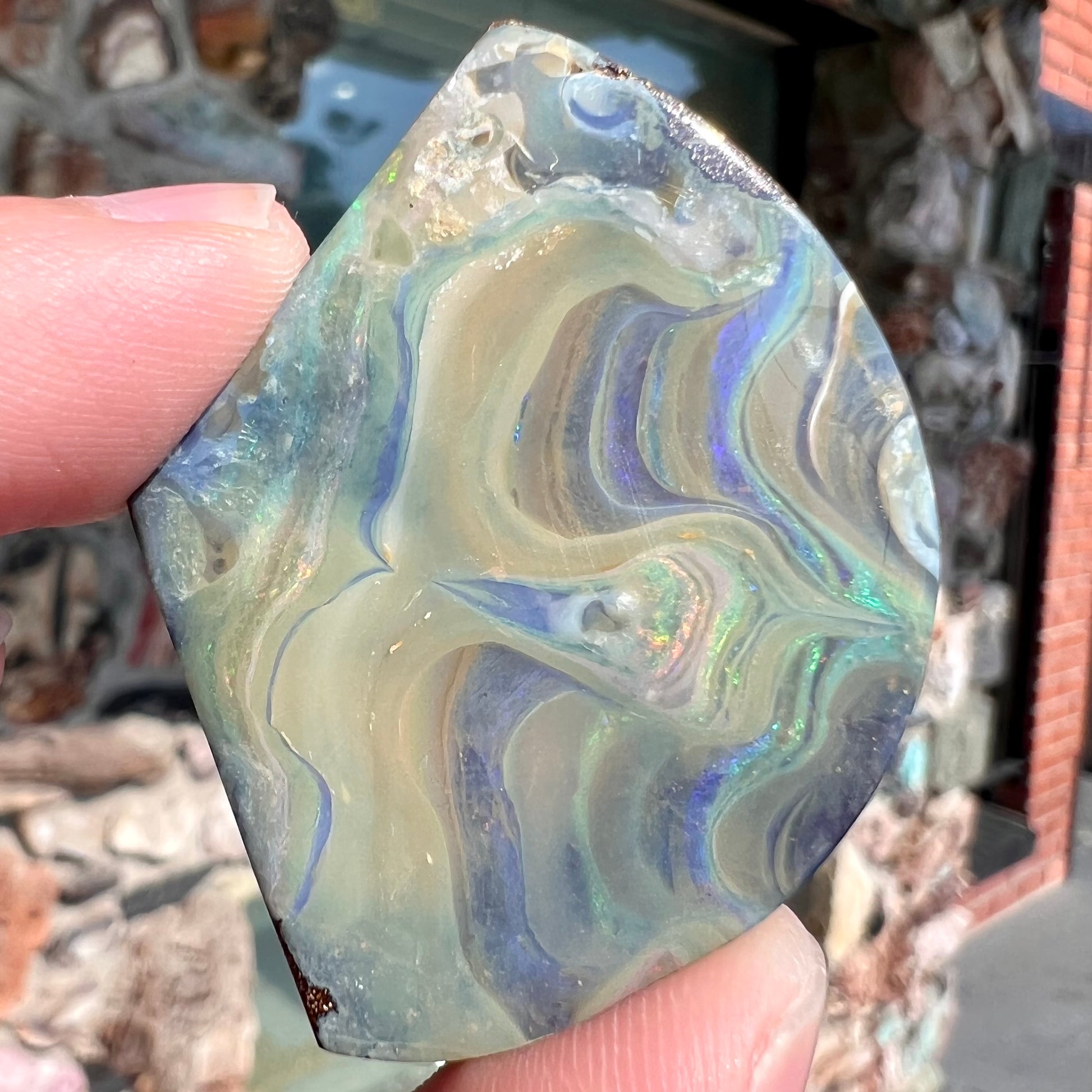 A polished, loose boulder opal stone from Queensland, Australia.  Fire colors are green, blue, purple, and salmon.