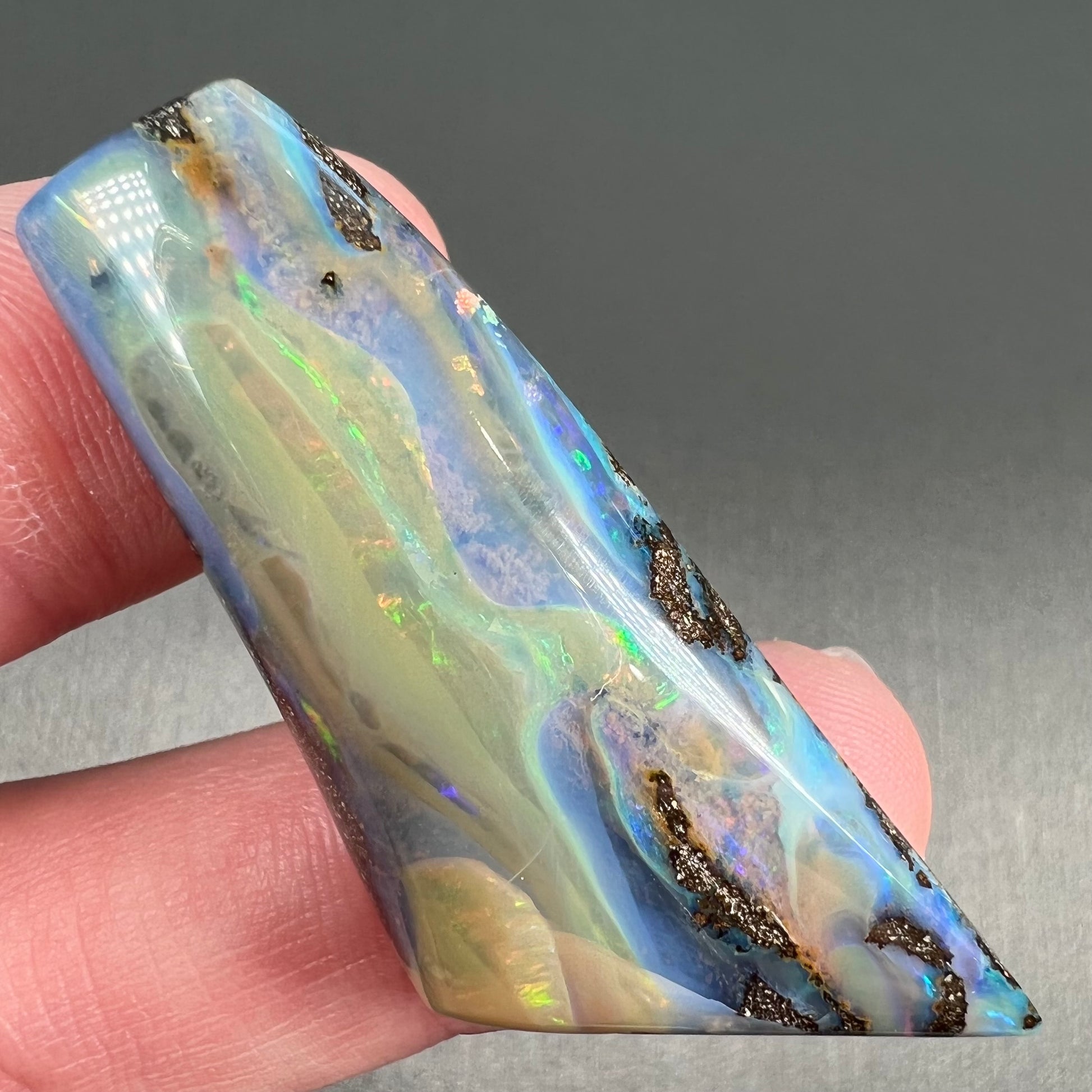 A freeform shaped, polished boulder opal stone from Queensland, Australia.  The stone has red, orange, green, and blue fire.