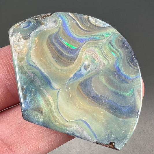 A polished, loose boulder opal stone from Queensland, Australia.  Fire colors are green, blue, purple, and salmon.