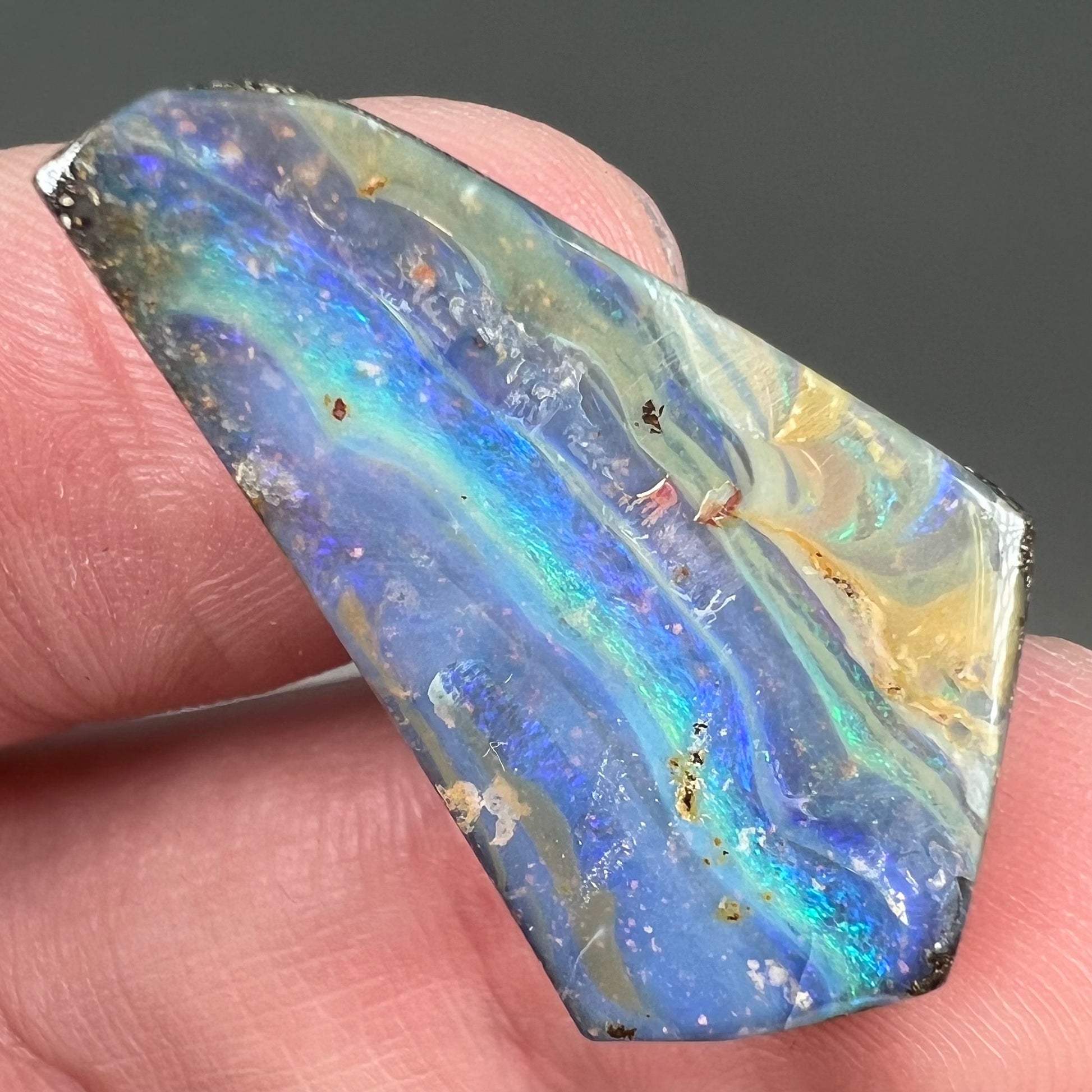 A loose, polished, freeform cut boulder opal stone from Queensland, Australia.