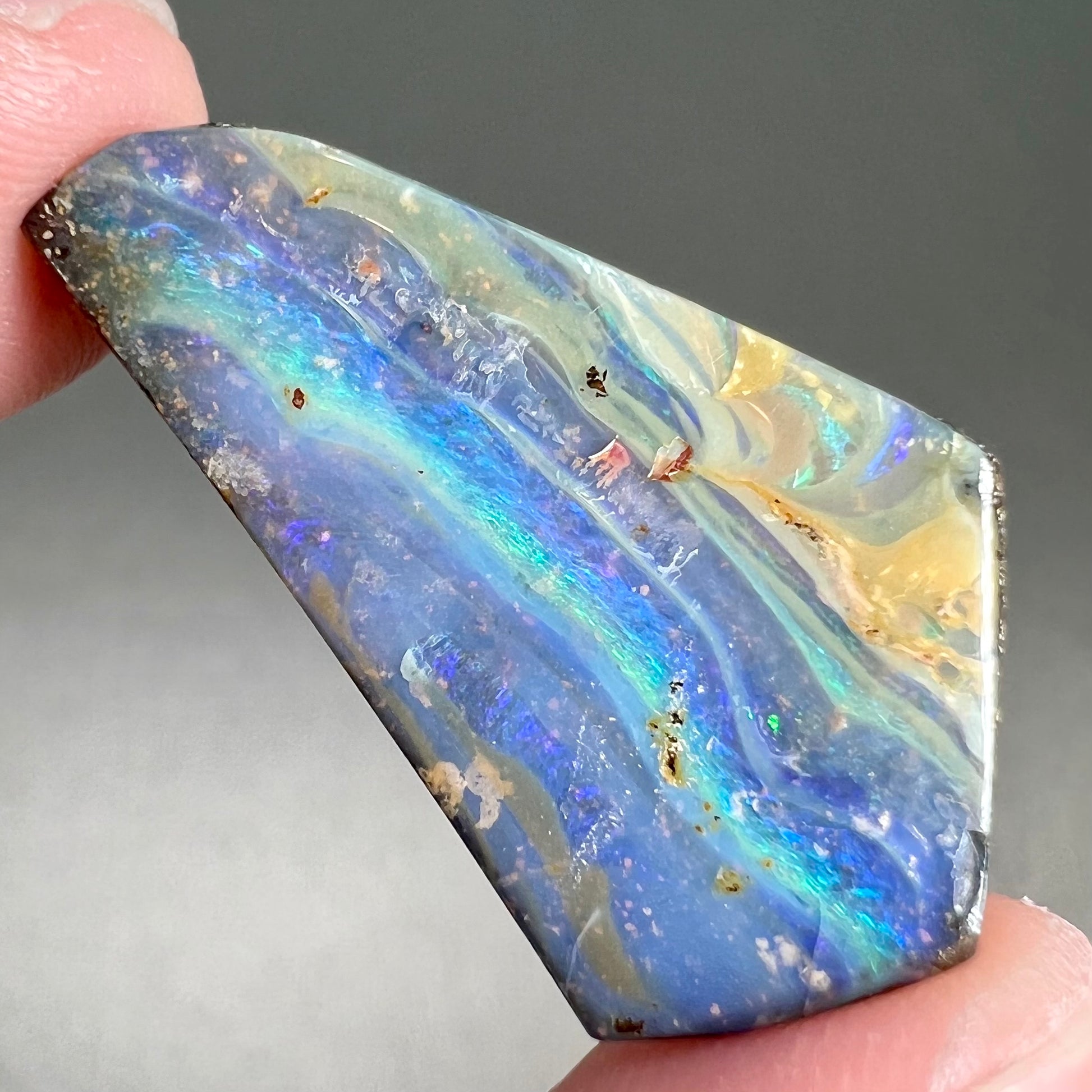 A loose, polished, freeform cut boulder opal stone from Queensland, Australia.