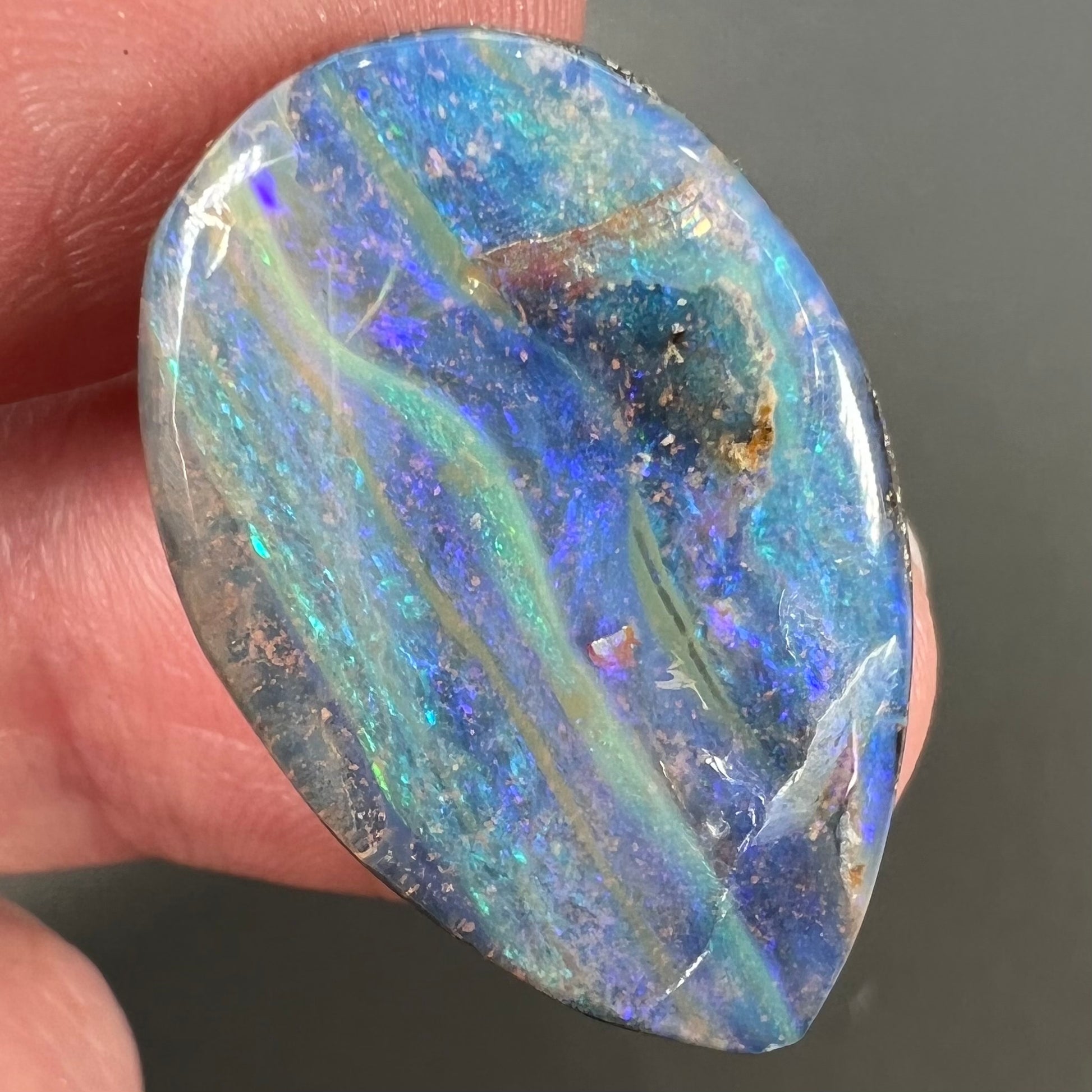 A loose, pear shaped Australian boulder opal stone.  The predominant colors are purple, green, and aqua.