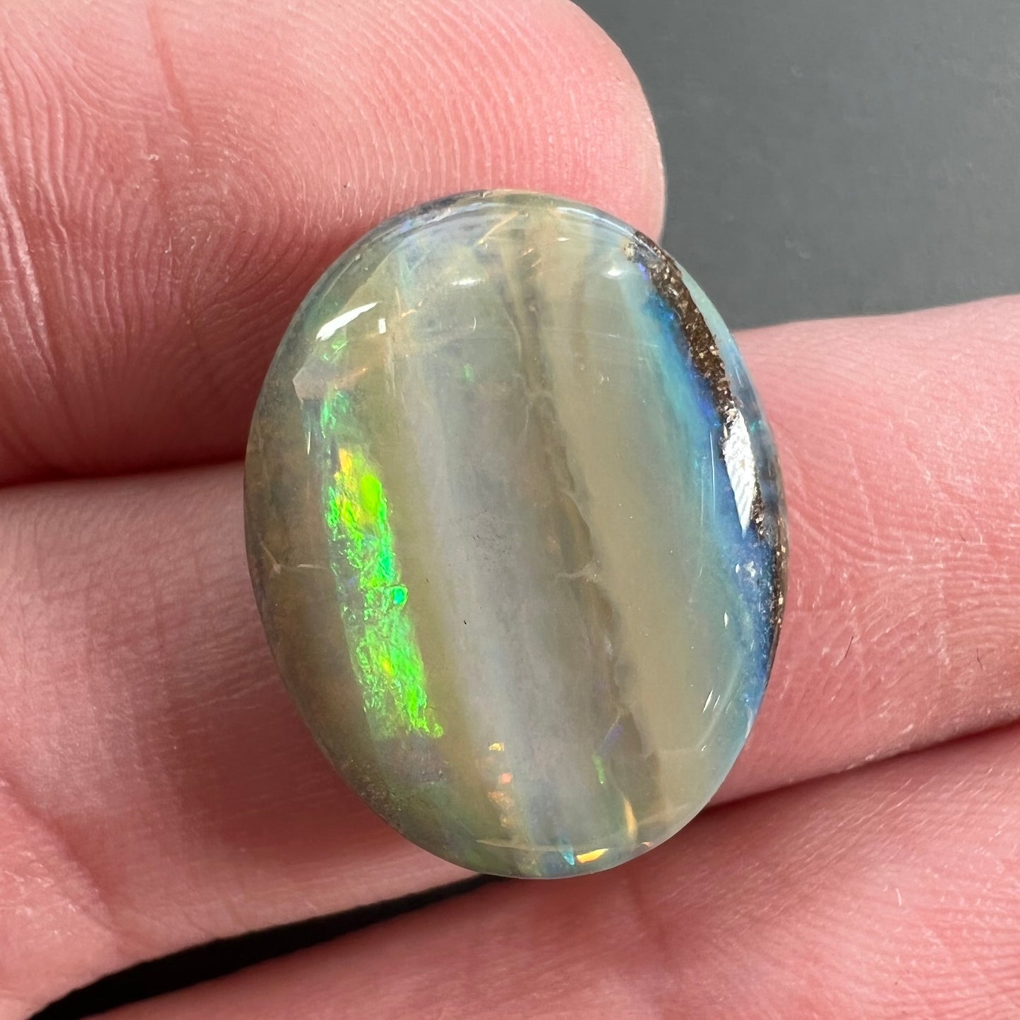 A loose, oval cabochon cut Quilpie boulder opal stone from Queensland, Australia.  The predominant color flash is green.