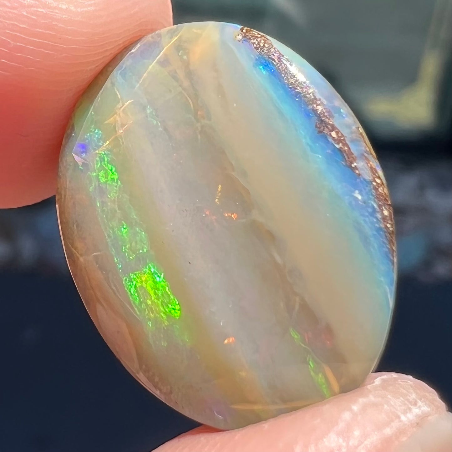 A loose, oval cabochon cut Quilpie boulder opal stone from Queensland, Australia.  The predominant color flash is green.