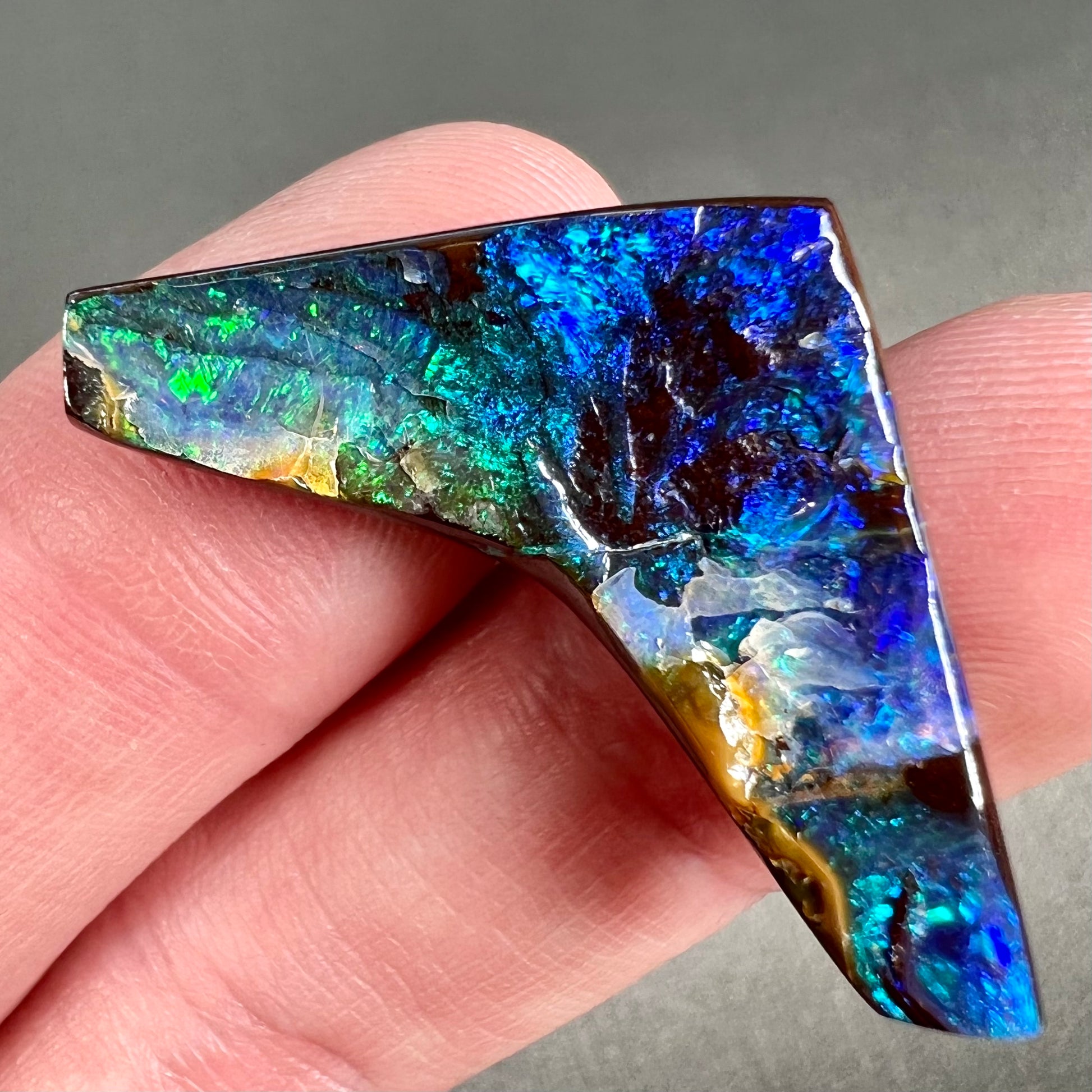 A loose, boomerang shaped boulder opal stone from Quilpie, Australia.  The stone is predominantly blue and green.