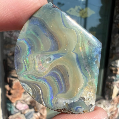 A polished, loose boulder opal stone from Queensland, Australia.  Fire colors are green, blue, purple, and salmon.