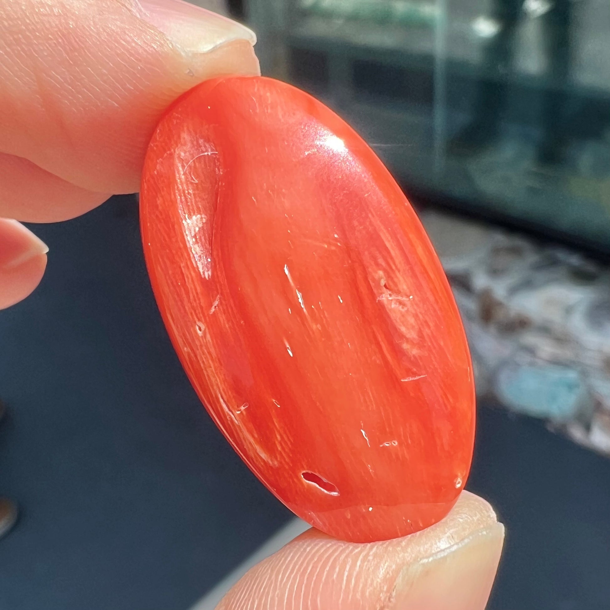 A large, loose red-orange coral cabochon that measures 1.2 inches by 0.7 inches.