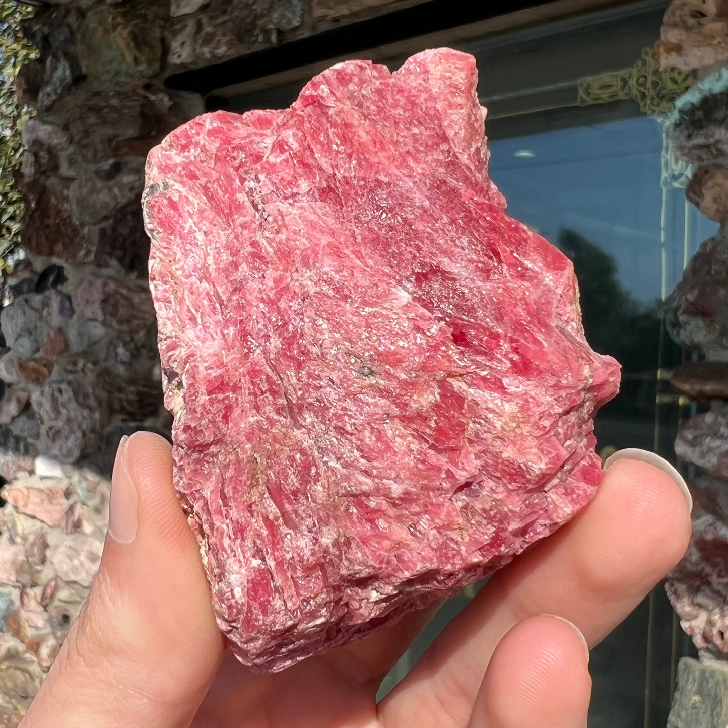 A rough pink rhodonite crystal specimen the size of a small fist.