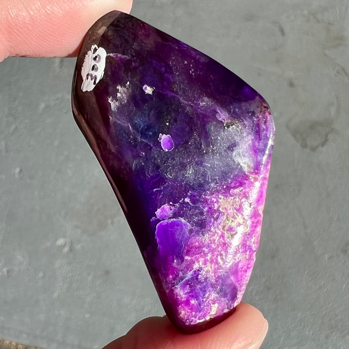 A loose, polished sugilite specimen displaying a blend of different shades of purple.