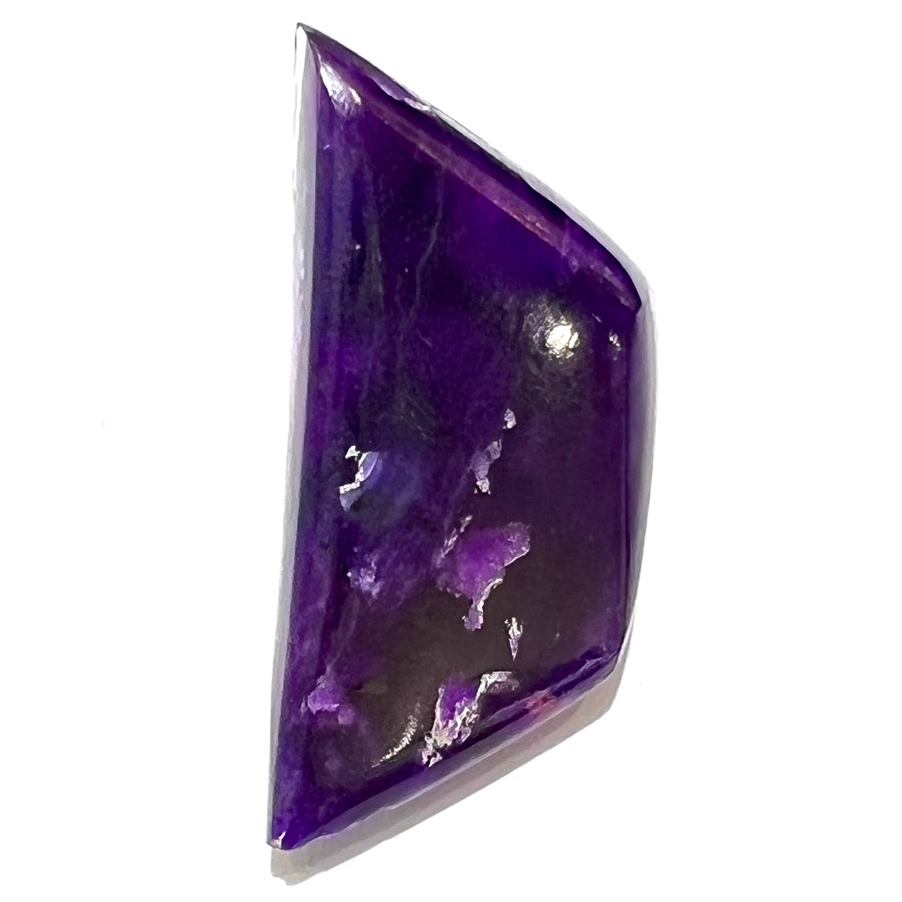 A freeform cabochon cut piece of dark purple sugilite.
