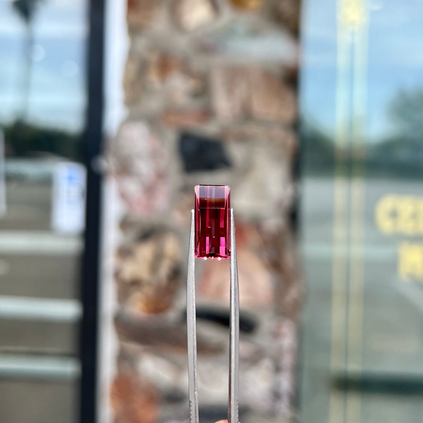 A loose, fantasy cut reddish colored tourmaline.  The cut reflects light in a way that resembles digital pixels on a screen.