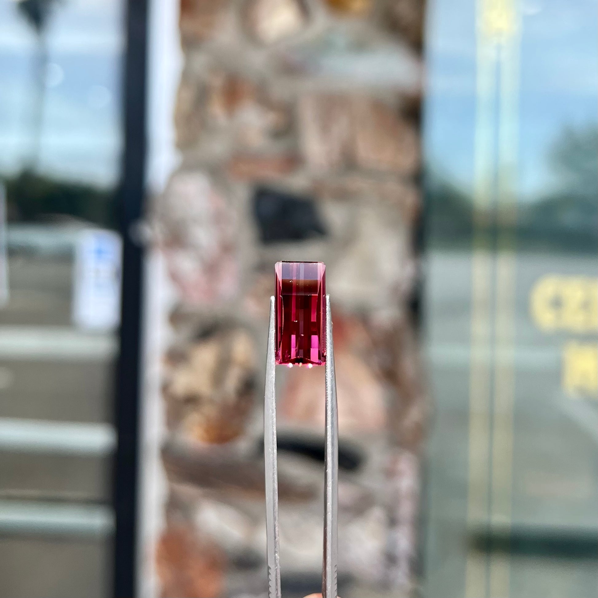 A loose, fantasy cut reddish colored tourmaline.  The cut reflects light in a way that resembles digital pixels on a screen.