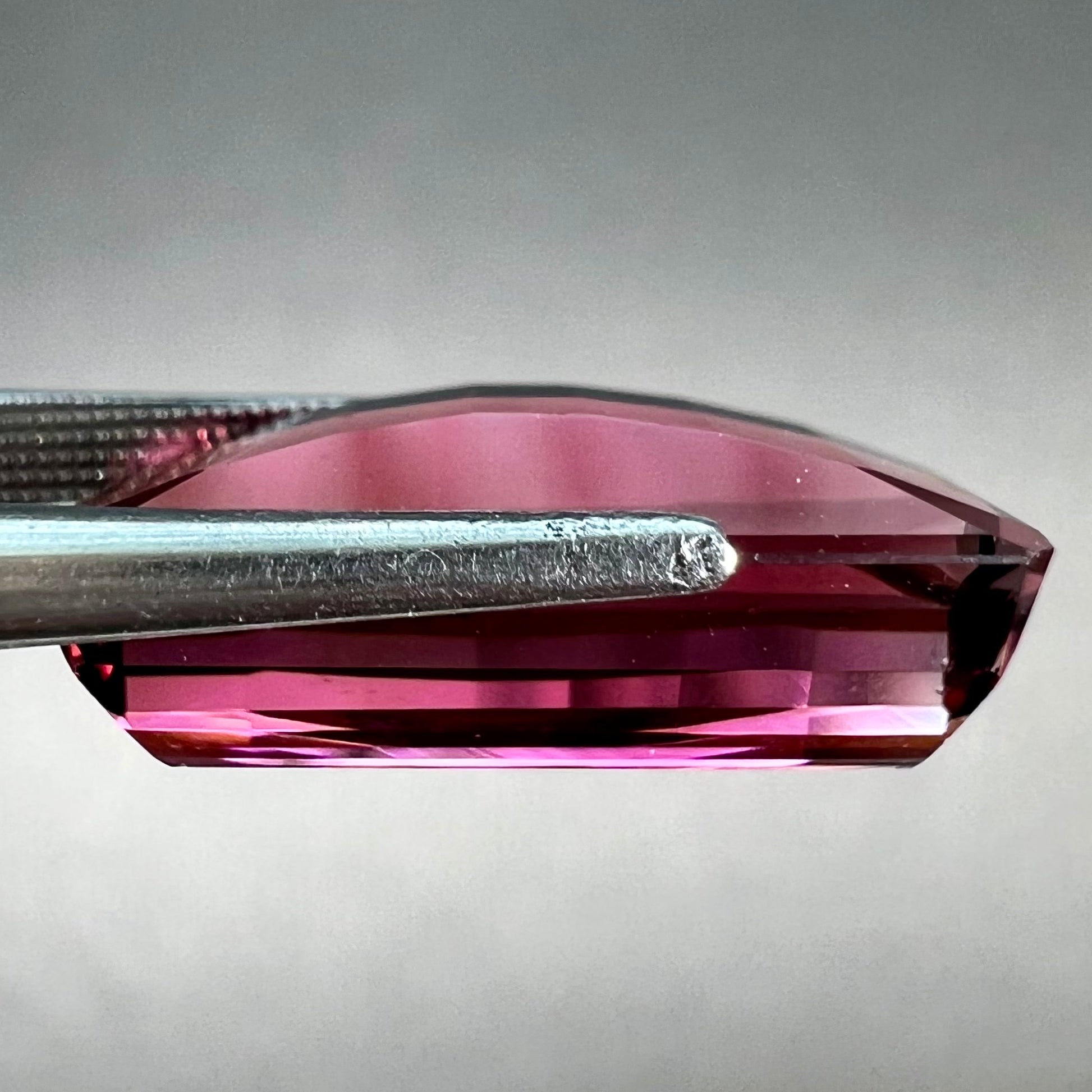 A loose, fantasy cut reddish colored tourmaline.  The cut reflects light in a way that resembles digital pixels on a screen.