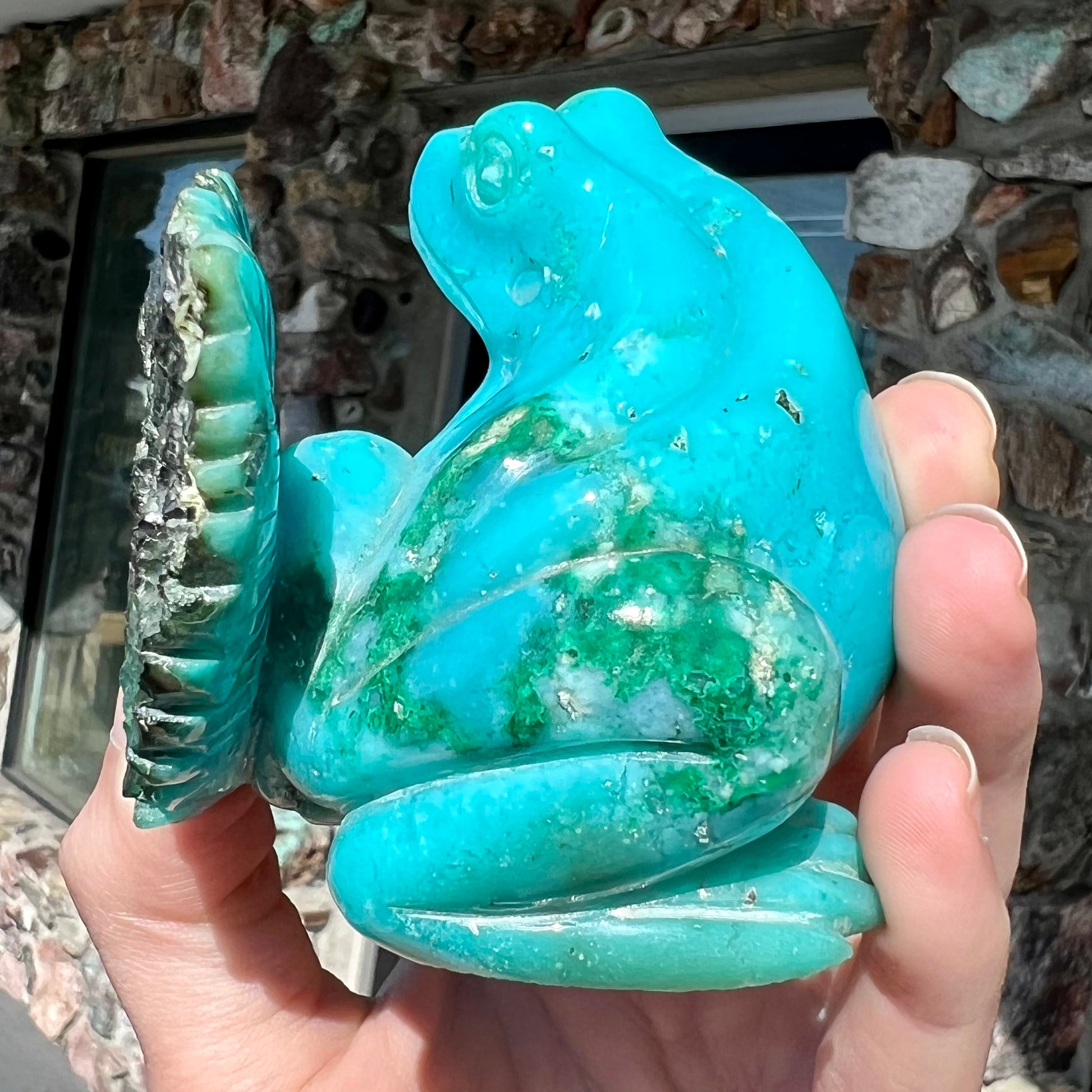 A stone frog peeking from behind a leaf carved from gem silica grade chrysocolla by artist, Ron Stevens.