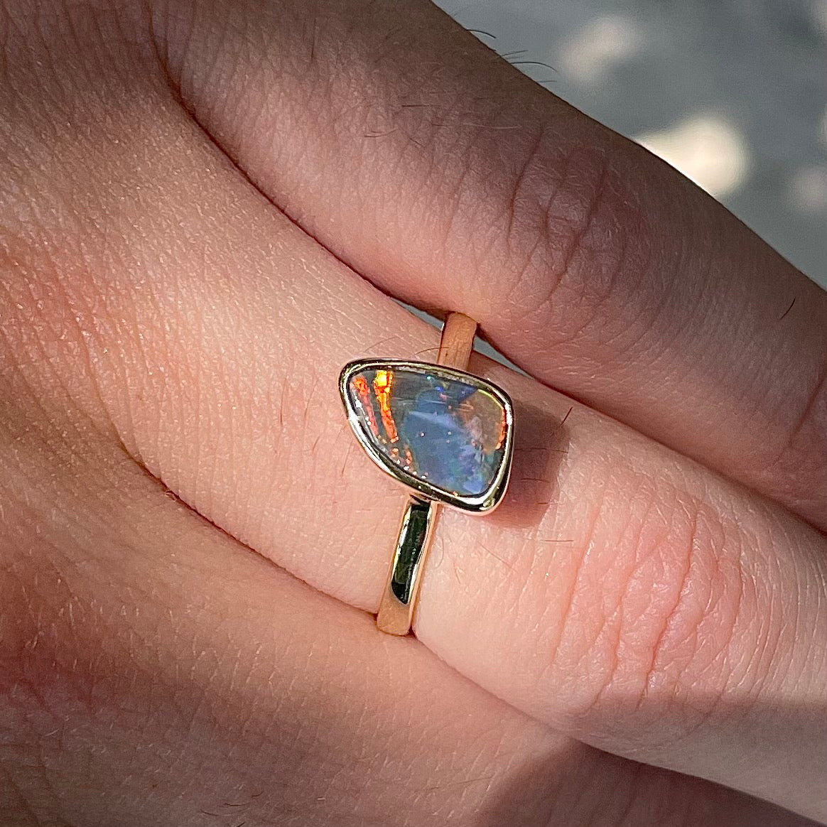 A handmade yellow gold solitaire ring bezel set with a Lightning Ridge red-on-black harlequin opal.