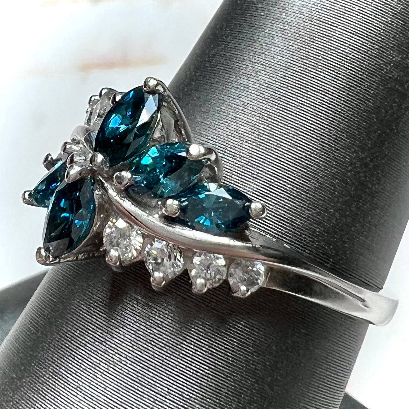 A white gold diamond cluster ring set with blue marquise cut and white round cut diamonds.
