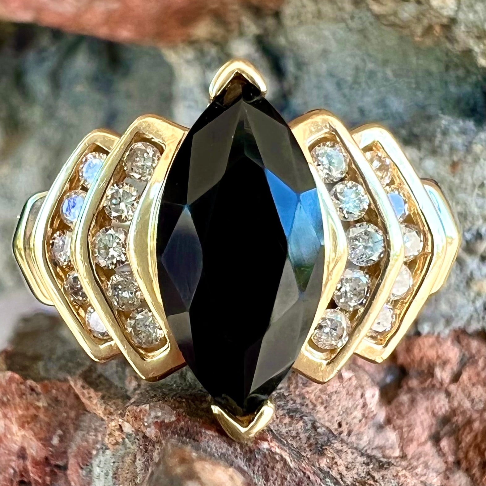 A gold, marquise cut black sapphire ring set with channel set diamond accents.