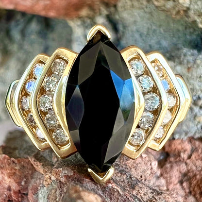 A gold, marquise cut black sapphire ring set with channel set diamond accents.