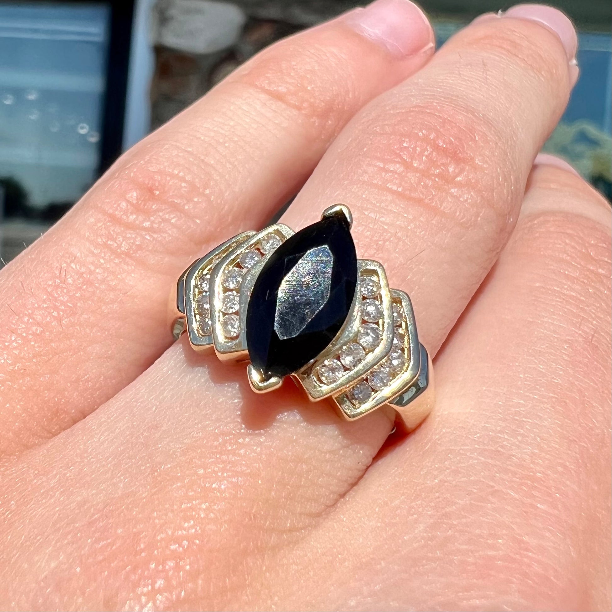 A gold, marquise cut black sapphire ring set with channel set diamond accents.