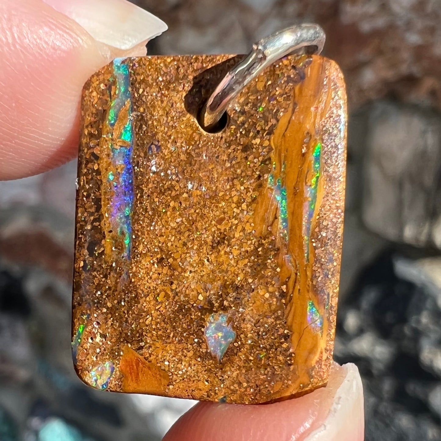 A drilled boulder opal stone with a sterling silver ring through the hole to be worn as a pendant.