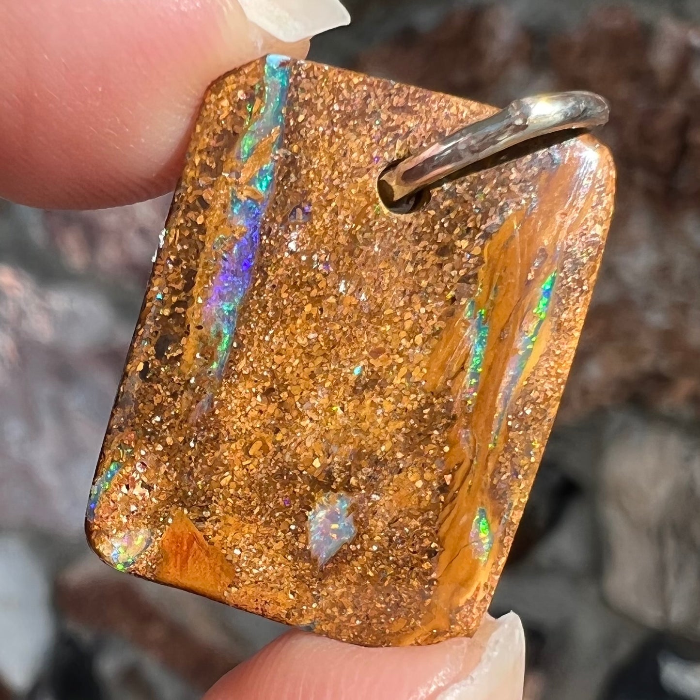 A drilled boulder opal stone with a sterling silver ring through the hole to be worn as a pendant.