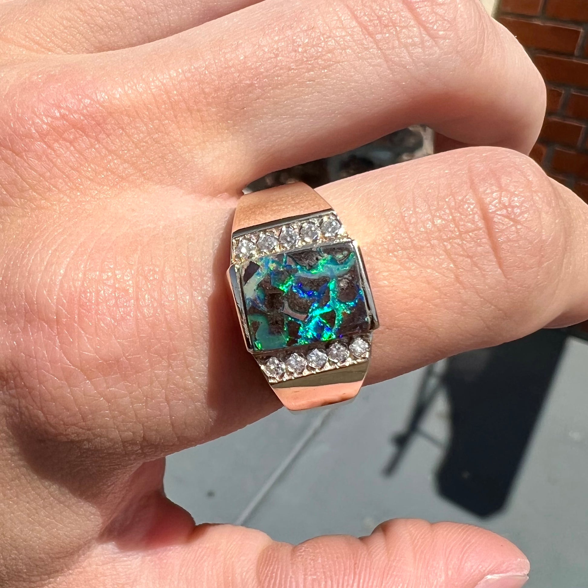 A men's gold boulder opal and diamond ring.  The opal shows blue and green colors.