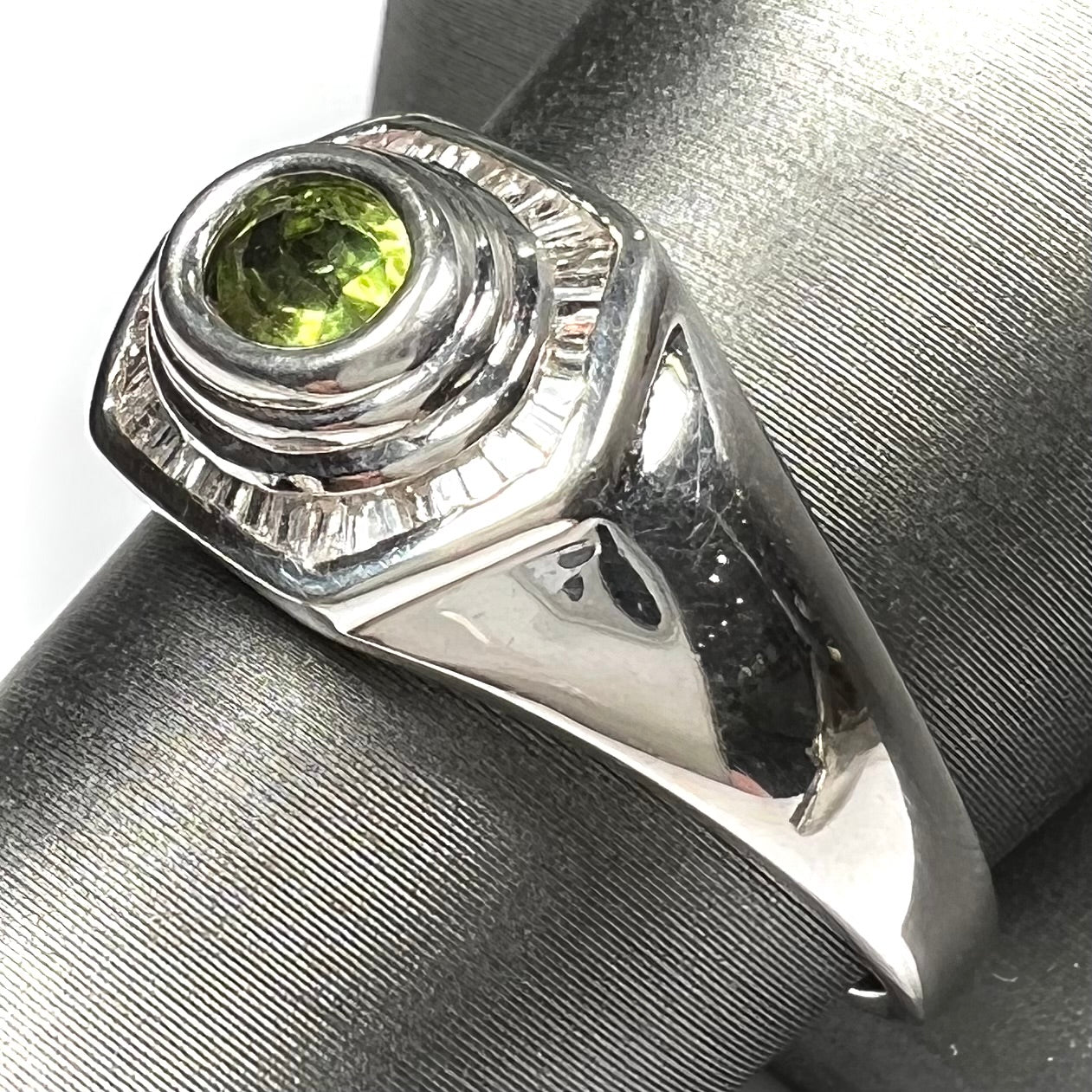 A sterling silver men's ring set with green peridot surrounded by baguette cut diamonds.