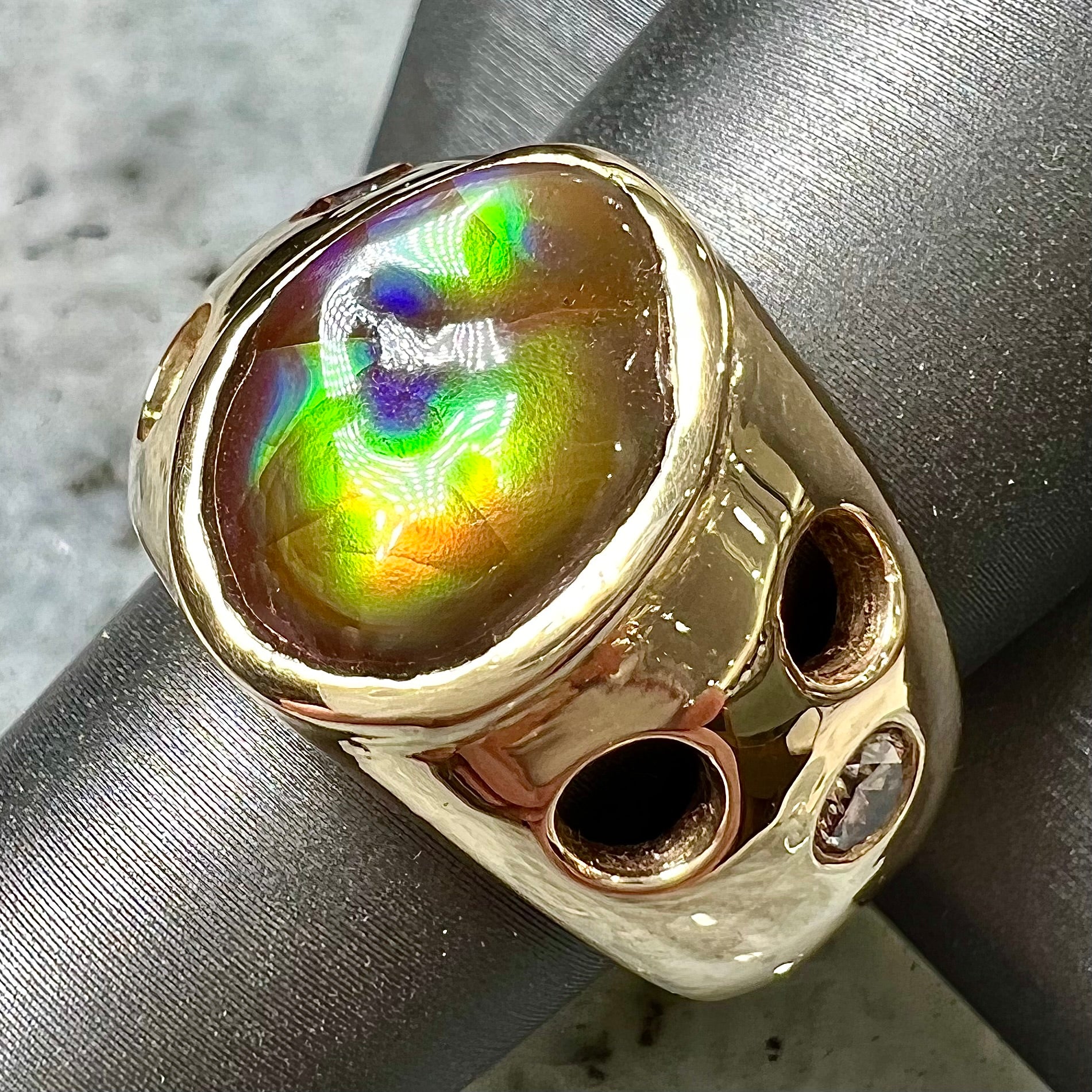 Men's rainbow fire agate ring set in yellow gold with champagne diamonds.  The ring style has holes.