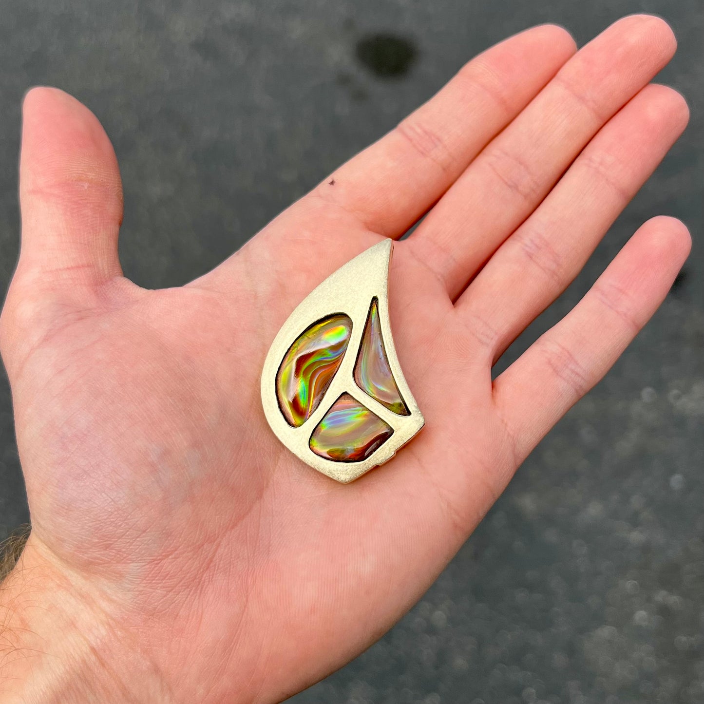 A men's gold pendant set with three fire agate stones.  The fire agate resembles an oil slick puddle.