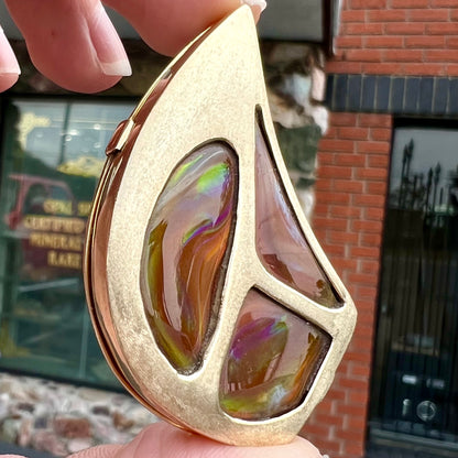 A men's gold pendant set with three fire agate stones.  The fire agate resembles an oil slick puddle.