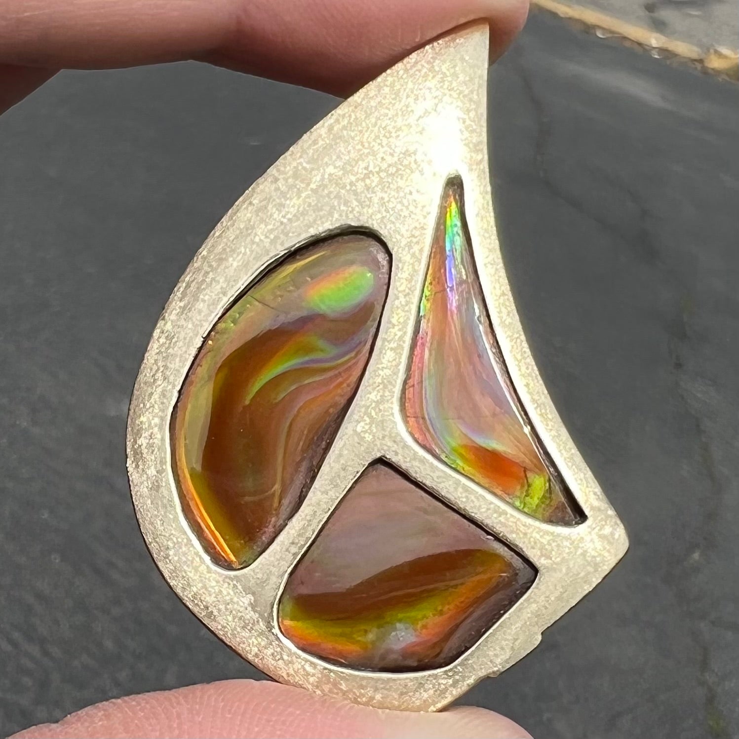 A men's gold pendant set with three fire agate stones.  The fire agate resembles an oil slick puddle.