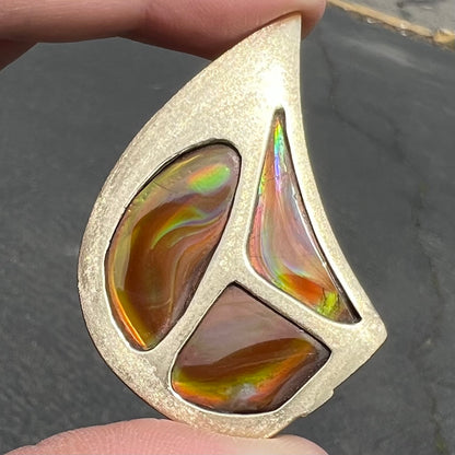 A men's gold pendant set with three fire agate stones.  The fire agate resembles an oil slick puddle.
