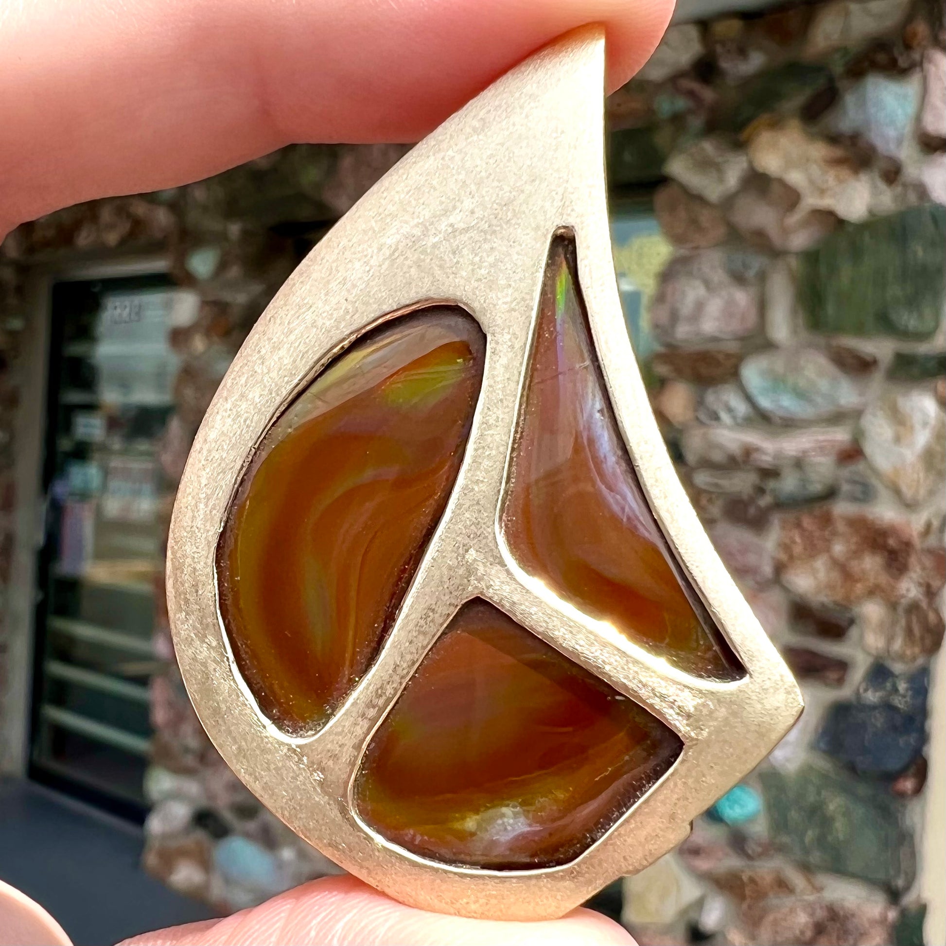 A men's gold pendant set with three fire agate stones.  The fire agate resembles an oil slick puddle.