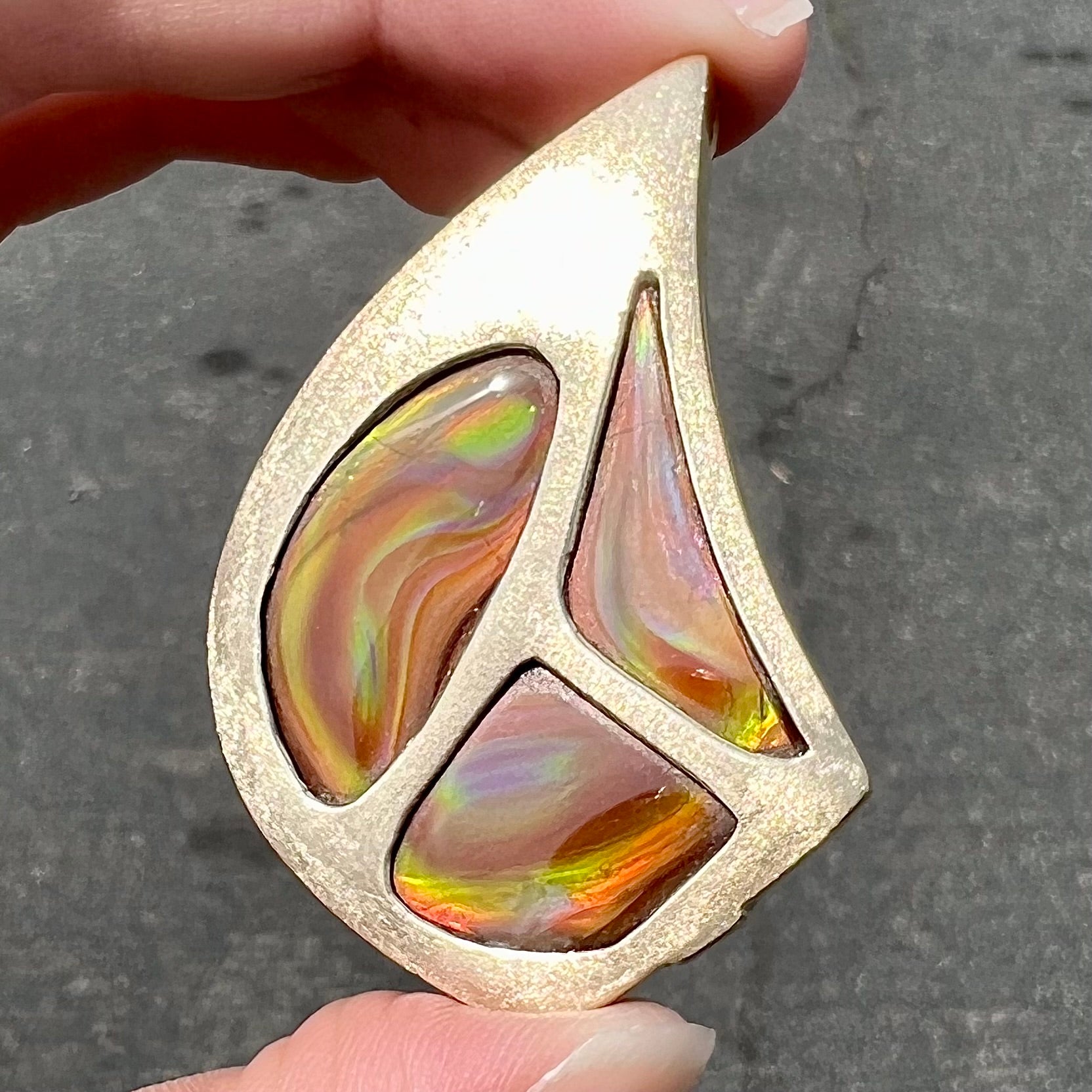 A men's gold pendant set with three fire agate stones.  The fire agate resembles an oil slick puddle.