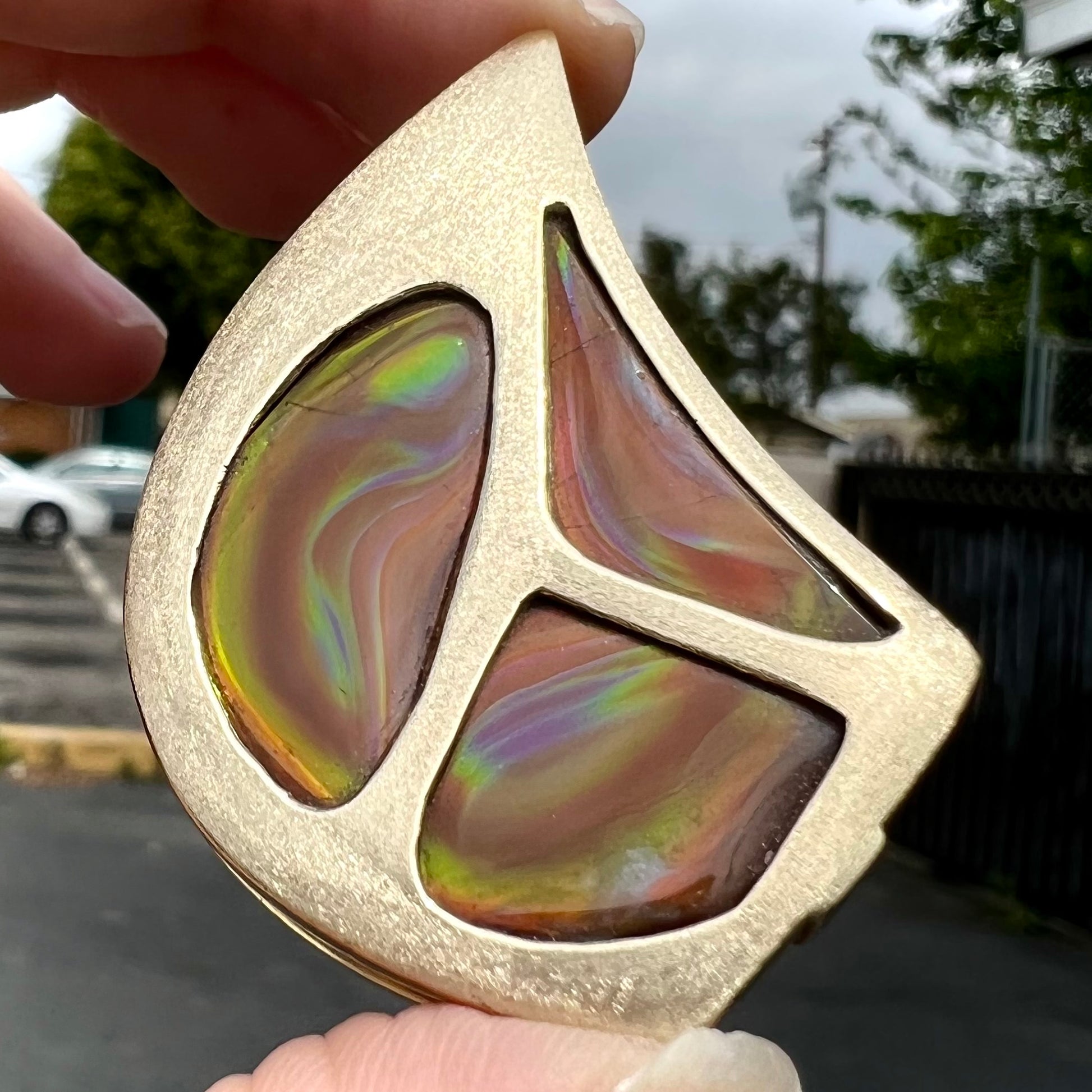 A men's gold pendant set with three fire agate stones.  The fire agate resembles an oil slick puddle.