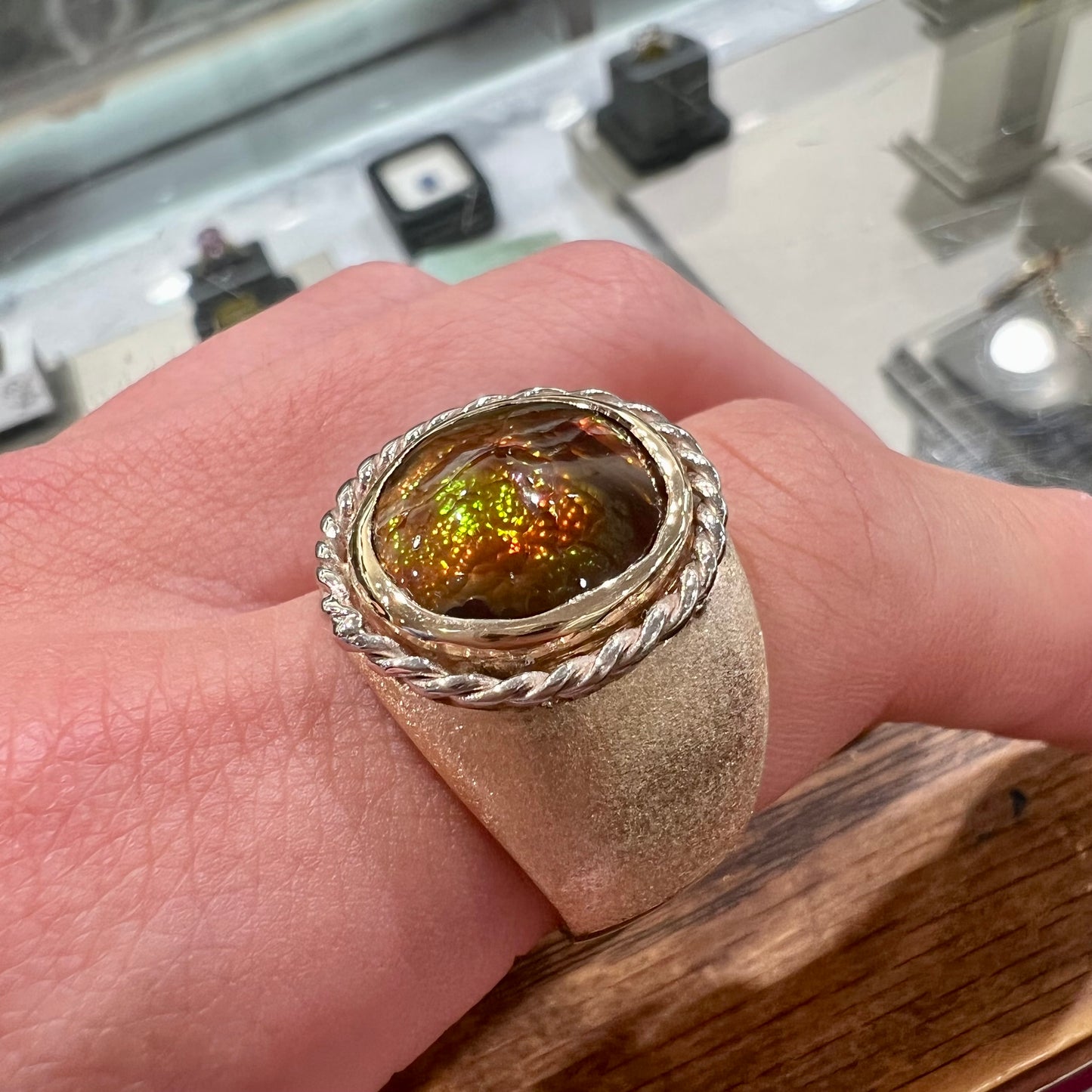 A men's matte finish textured gold fire agate ring.  There is a gold rope bezel around the oval cabochon cut stone.
