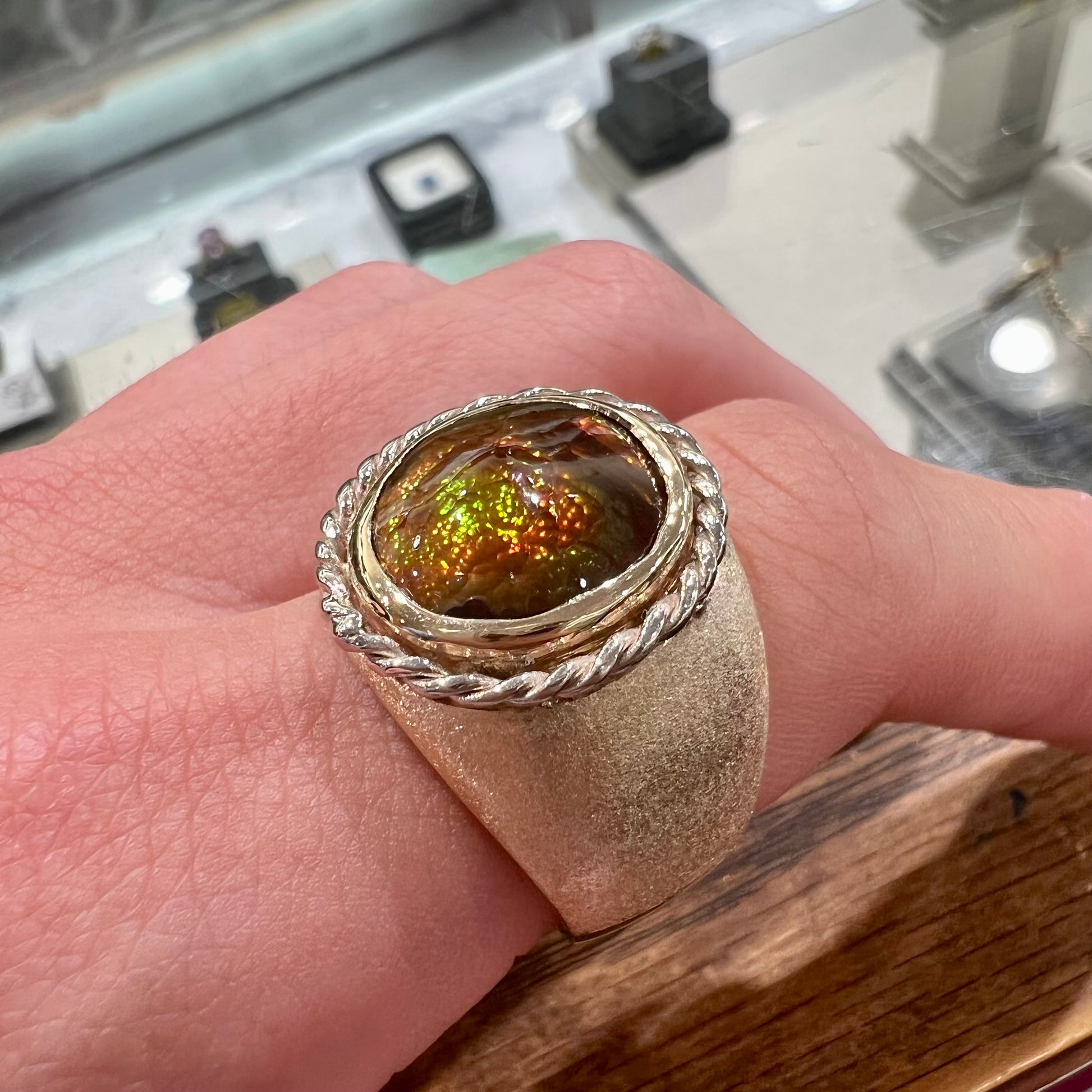A men's matte finish textured gold fire agate ring.  There is a gold rope bezel around the oval cabochon cut stone.
