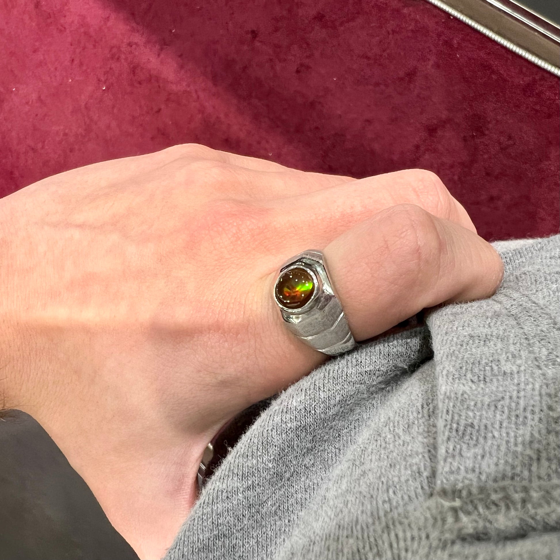 A round cabochon cut red and green fire agate set in a brushed metal white gold men's ring.