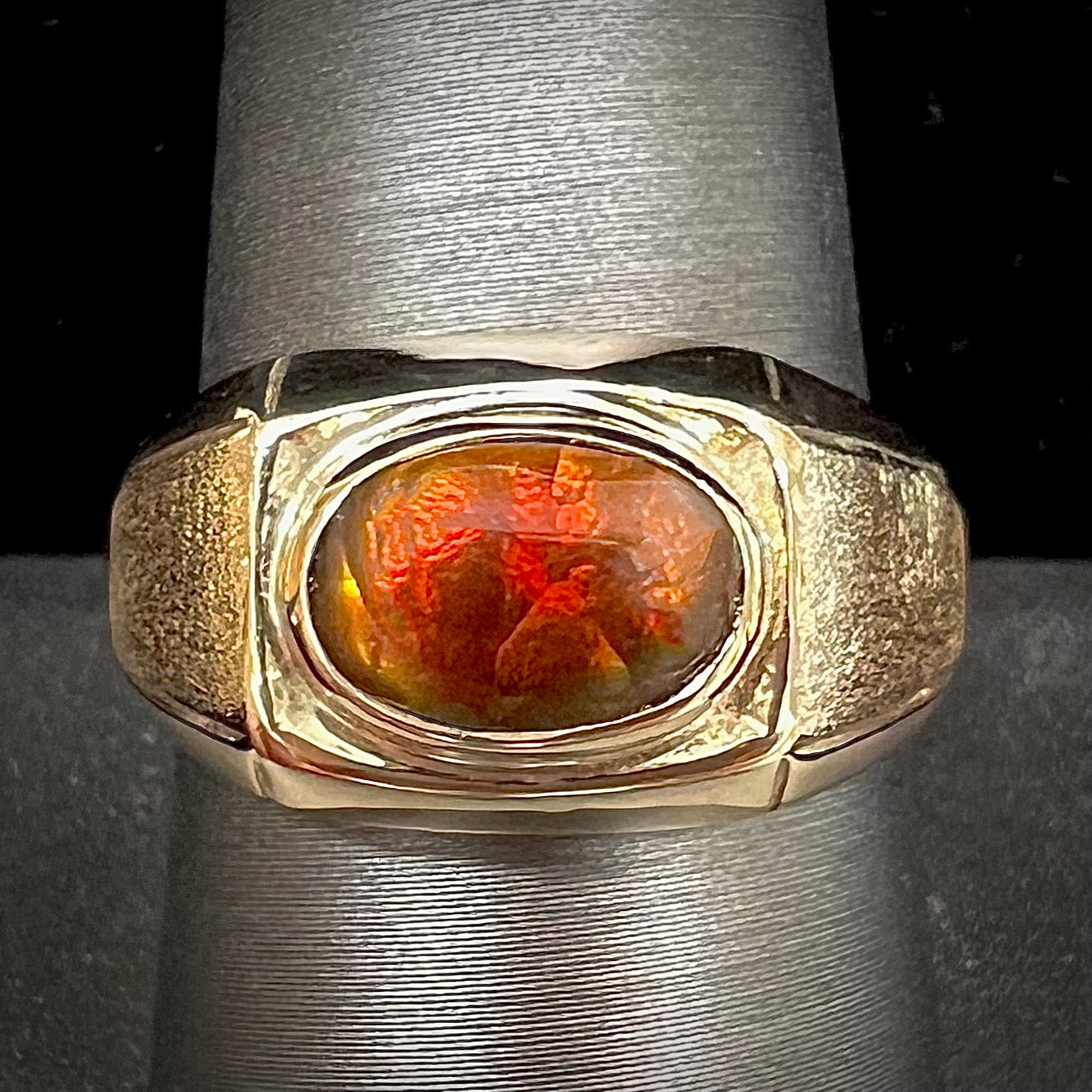 A yellow gold men's fire agate solitaire ring.  The fire agate is red with green undertones.