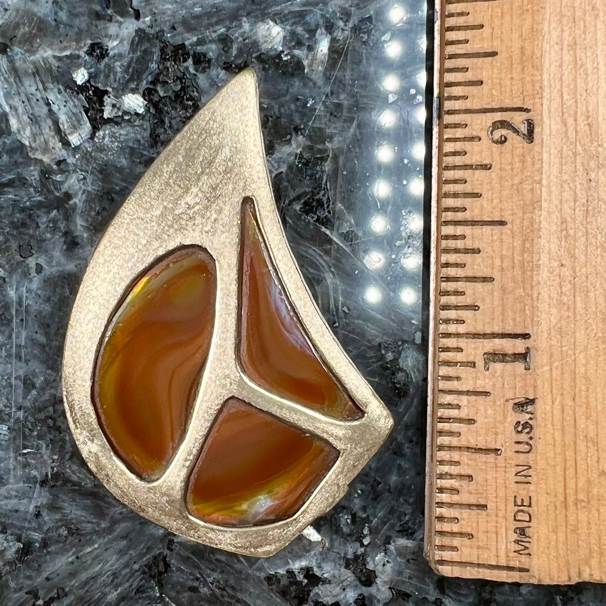 A men's gold pendant set with three fire agate stones.  The fire agate resembles an oil slick puddle.