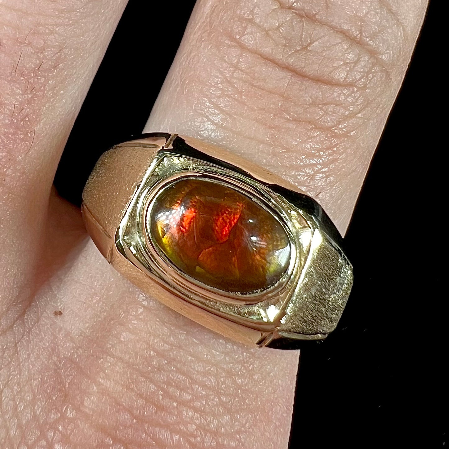 A yellow gold men's fire agate solitaire ring.  The fire agate is red with green undertones.