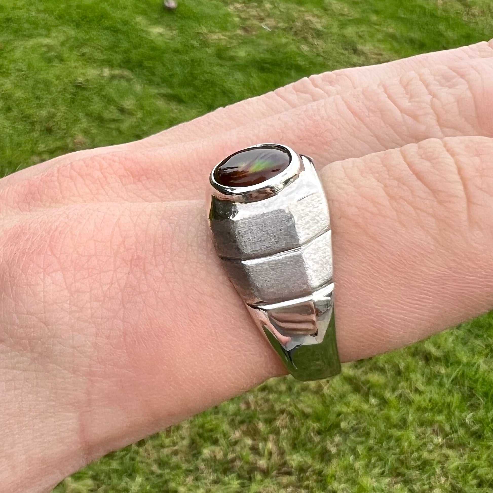 A round cabochon cut red and green fire agate set in a brushed metal white gold men's ring.