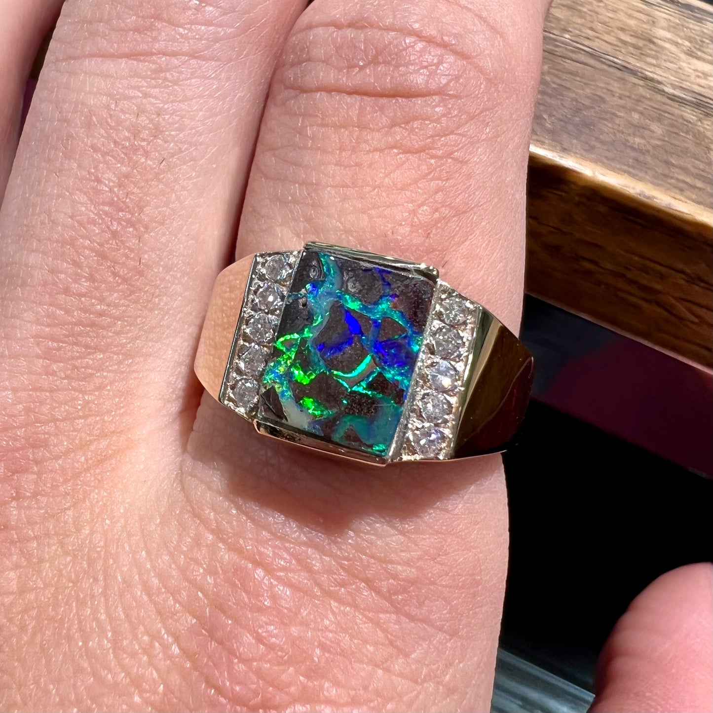 A men's gold boulder opal and diamond ring.  The opal shows blue and green colors.