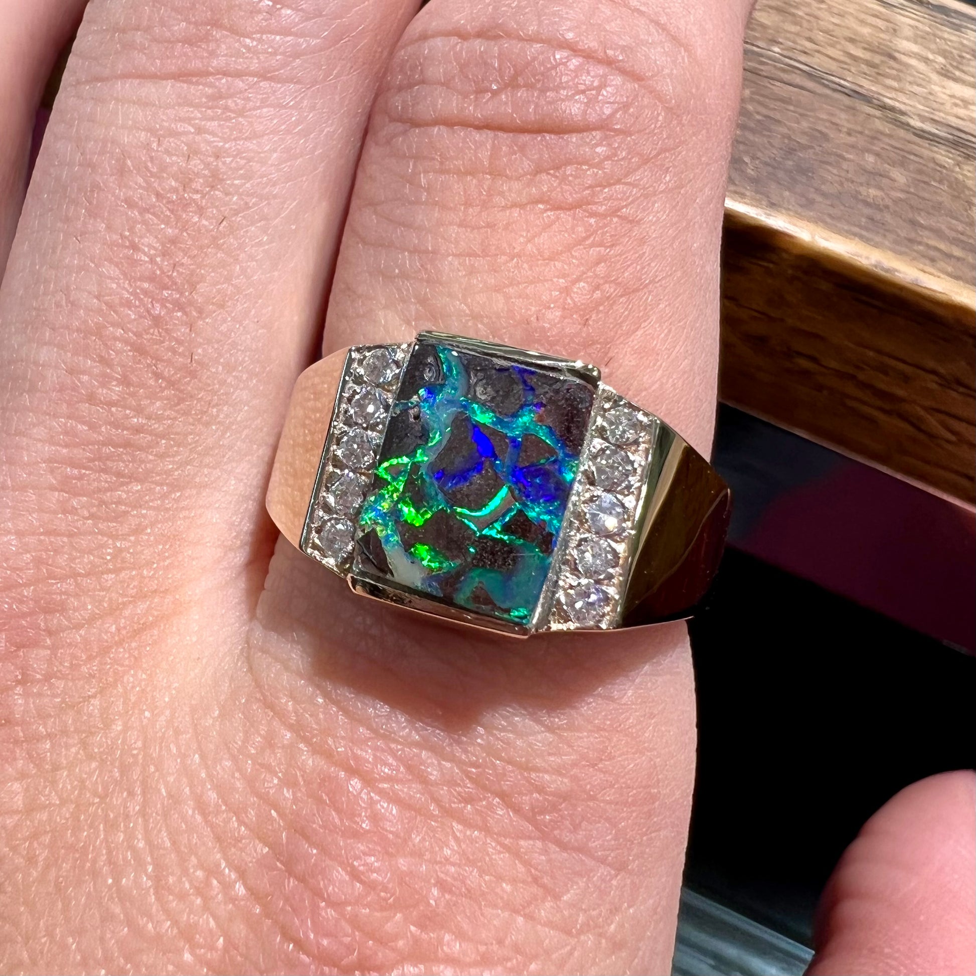 A men's gold boulder opal and diamond ring.  The opal shows blue and green colors.