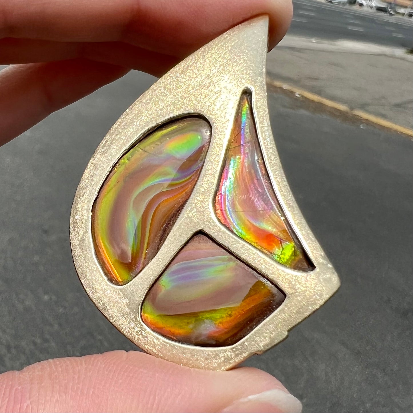 A men's gold pendant set with three fire agate stones.  The fire agate resembles an oil slick puddle.