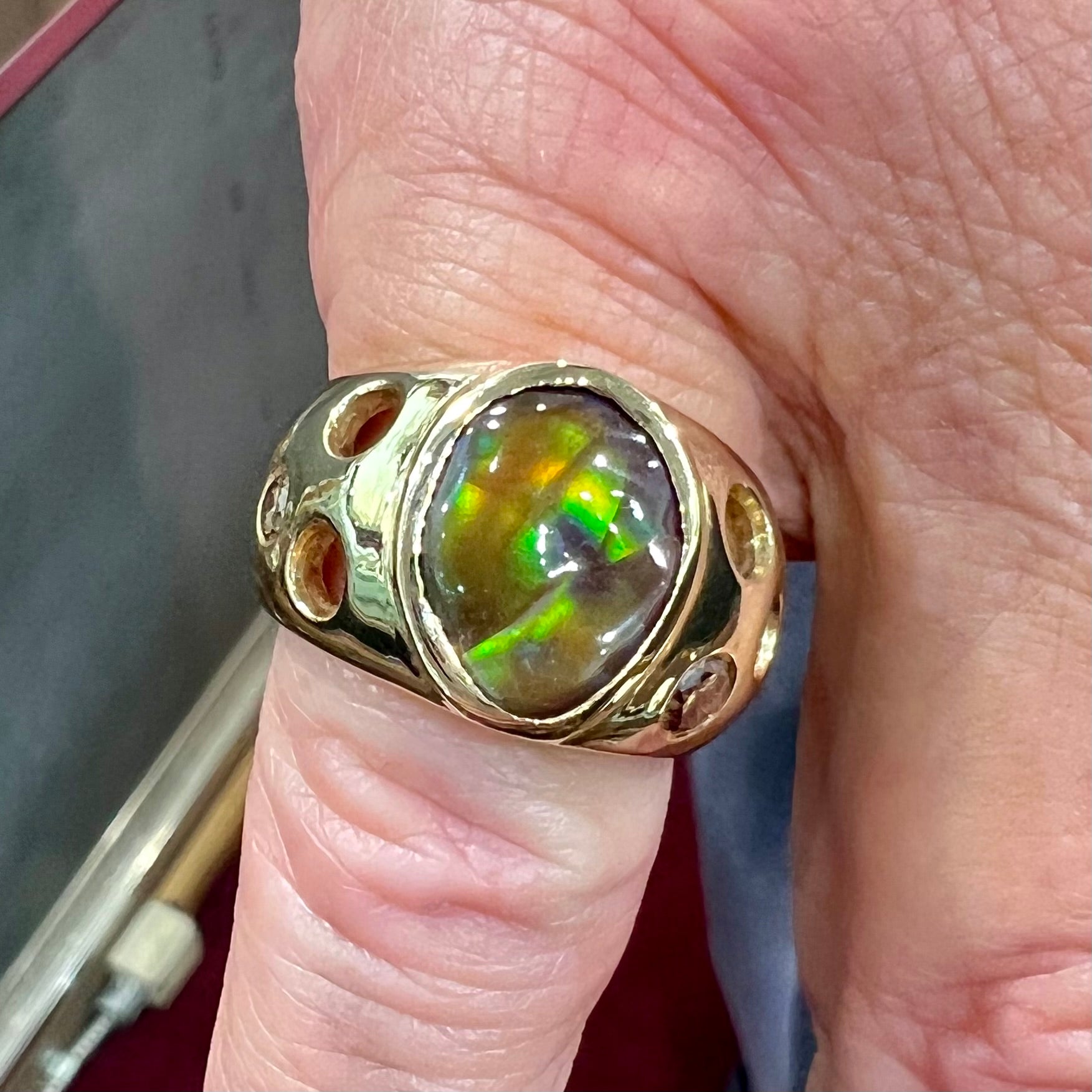 Men's rainbow fire agate ring set in yellow gold with champagne diamonds.  The ring style has holes.