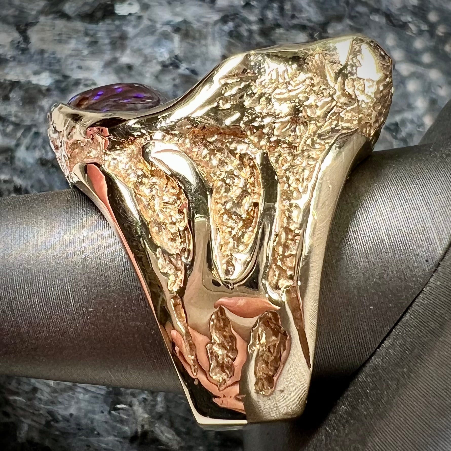 A men's Deer Creek fire agate solitaire ring cast in yellow gold.  The stone is predominantly purple.