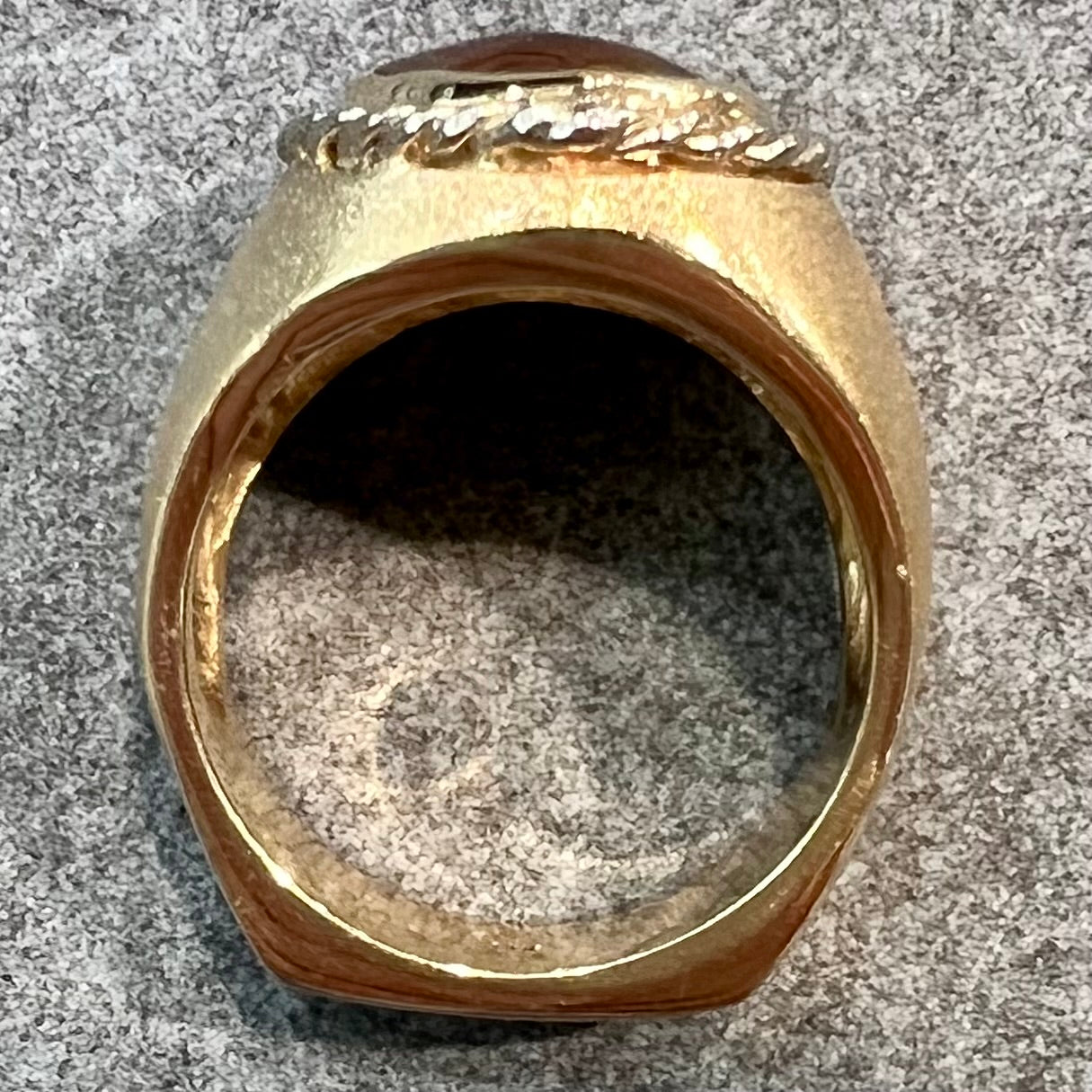 A men's matte finish textured gold fire agate ring.  There is a gold rope bezel around the oval cabochon cut stone.