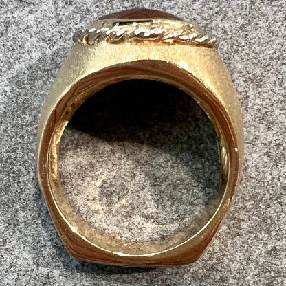 A men's matte finish textured gold fire agate ring.  There is a gold rope bezel around the oval cabochon cut stone.